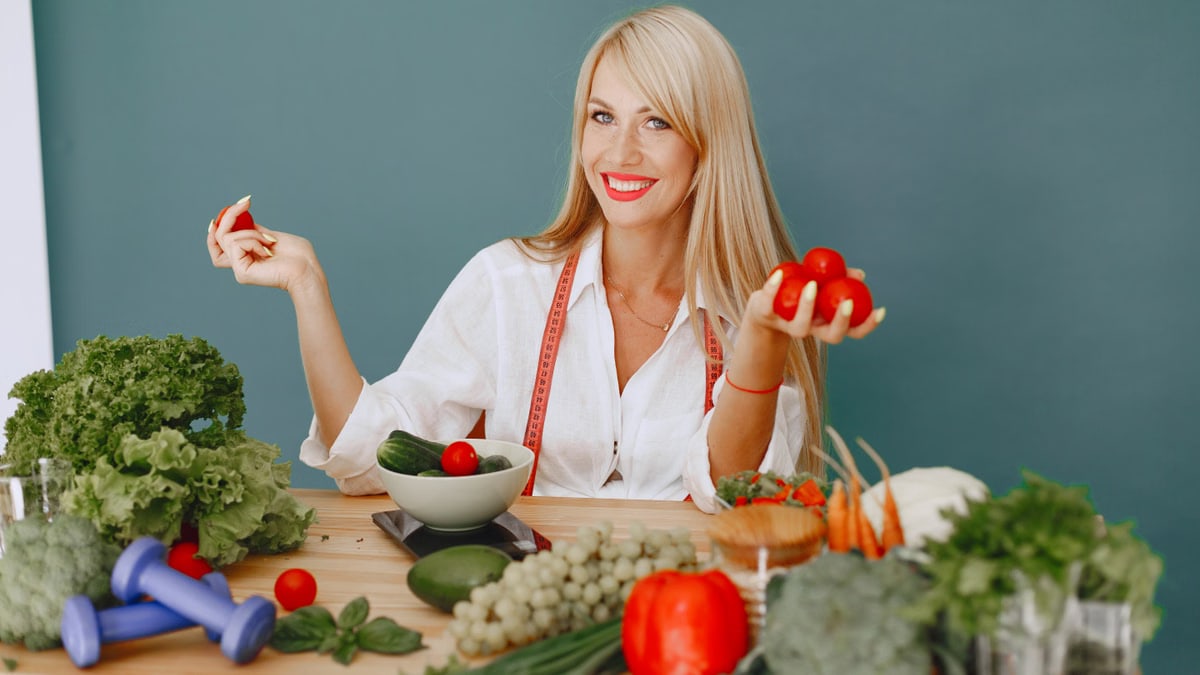 Healthy lifestyle concept with woman holding tomatoes and surrounded by fresh vegetables in a studio setting.