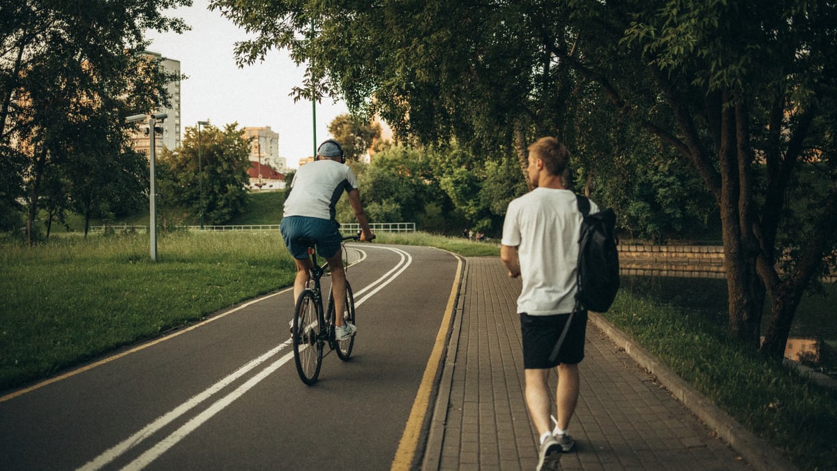A cyclist and a walker enjoy a peaceful park trail surrounded by greenery.